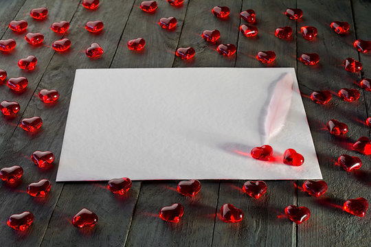 Red hearts made of glass on wooden background. White sheet of paper as a free space for text.