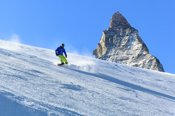Fototapeta na wymiar Male snowboarder on the slope with Matterhorn mountain peak on background