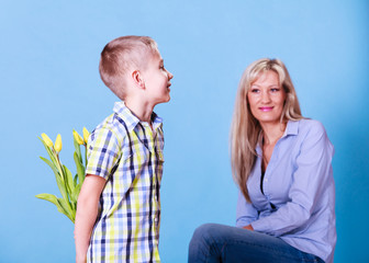 Little boy with mother hold flowers behind back.
