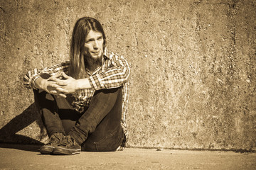 Man long haired sitting alone sad on grunge wall