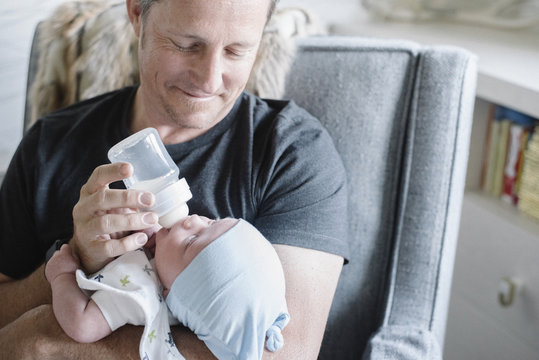 Father cradling and bottle feeding newborn baby