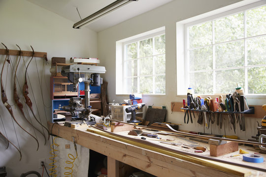 A workshop bench with components and tools, and finished articulated bows hanging on the wall. 