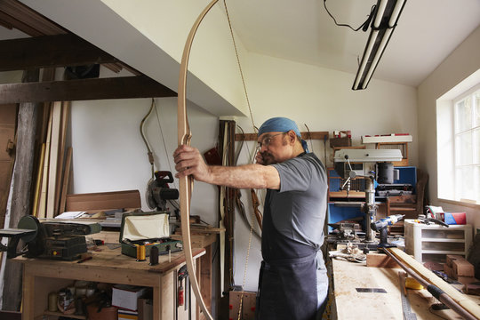 A man testing out a hand made bow by pulling the bow string. 