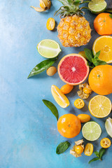 Variety of whole and sliced citrus fruits pineapple, grapefruit, lemon, lime, kumquat, clementine and physalis with mint over blue wooden background. Top view with space. Healthy eating, dieting