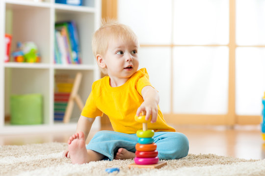 Portrait of cute kid boy assembling colorful pyramid toy on floor at living room