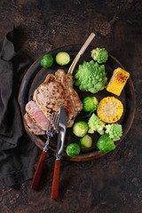 Sliced grilled veal tomahawk steak with vegetables brussels sprouts, romanesco and corn cobs served...