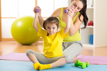 Fototapeta premium Woman helps child doing fitness exercises with dumbbells in gym