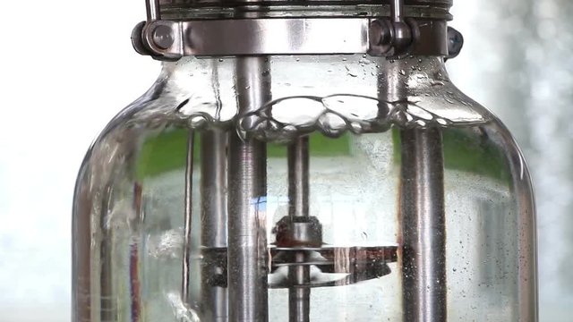 A top of the laboratory glass bioreactor filled with water. Central detail rotates and agitates the water. Lockdown. Close up.