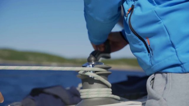 A man on a boat is unwinding the rope. He is wearing a blue anorak. The sailing boat is sailing on the Adriatic Sea on a beautiful summer day.
