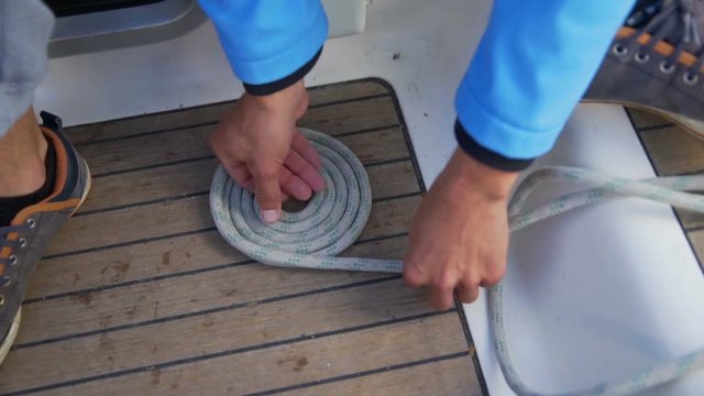 A sailor is trying to organize a rope in a nice circle. He is doing it very precisely and slowly. He is sitting on the sailing boat's deck.
