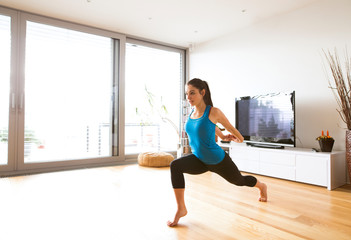 Young woman exercising at home, stretching legs and arms.