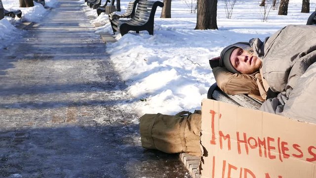 

4K.Young man with cardboard in  winter city park. Homeless life  slider shot
