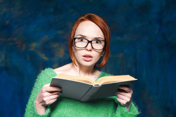 beautiful red-haired girl in a green sweater and glasses reading  book