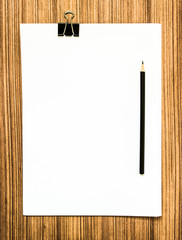 Blank paper with pencil on wood table.top view shot.