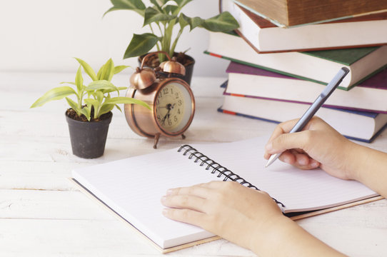 Hand Writing Paper On Desk And Work Place With Clock, Book And Palnt