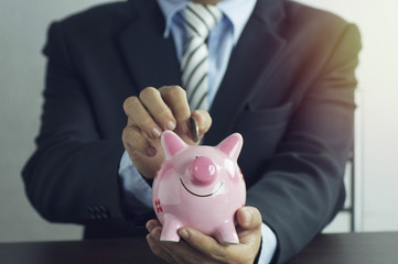 hand of businessman put money on pink of piggy bank , concept in growth, save and investment in business