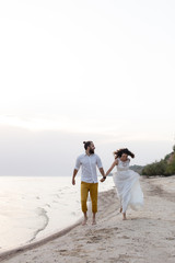 Beach honeymoon couple holding hands walking on white sand beach. Newlyweds happy in love relaxing on summer holidays. Travel vacation concept.