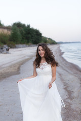 Fototapeta na wymiar Beautiful young brunette woman in white long dress at the sea shore