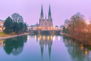 Fototapeta na wymiar Picturesque foggy Reformed Saint Paul church with mirror reflections in the river Ile during morning blue hour, Strasbourg, Alsace, France