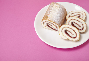 A strawberry jam Swiss roll cake on a bright pink background with blank space at side