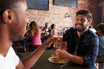 Friends Eating Out In Sports Bar With Screens In Background