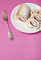 A strawberry jam Swiss roll cake on a bright pink background with fork and blank space below