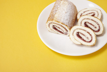 A strawberry jam Swiss roll cake on a bright yellow background with blank space at side