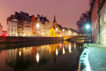 Picturesque quay and church of Saint Nicolas with mirror reflections in the river Ile during morning blue hour, Strasbourg, Alsace, France