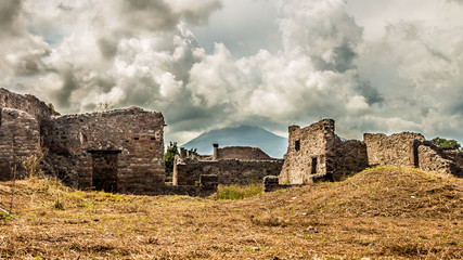 Ancient ruins with dangerous volcano on the horizon. Ruins of an ancient city of Pompeii near Naples and the Mount Vesuvius rises its summit on the horizon. 