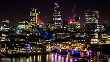 Fototapeta na wymiar Modern big city tall skyscrapers in the industrial business city at night. Capital of finances City of London at night. Long and curvy lights reflections in the river Thames.