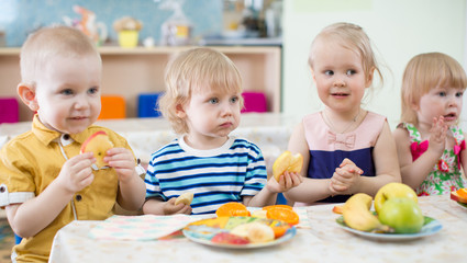 Obraz na płótnie Canvas funny kids eating fruits in kindergarten dinning room