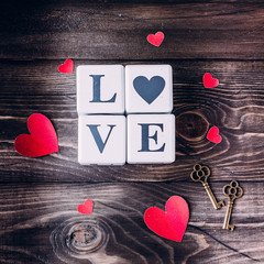 Message love spelled in wooden blocks, metal key and paper hearts. Top view with copy space