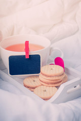 Breakfast in bed in Valentines day. Cup of tea and cookies. Message love spelled in wooden blocks. Black board for Message,copy space .