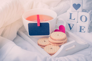 Breakfast in bed in Valentines day. Cup of tea and cookies. Message love spelled in wooden blocks. Black board for Message,copy space .