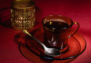 The Cup, brewed coffee, on a transparent saucer lies a teaspoon