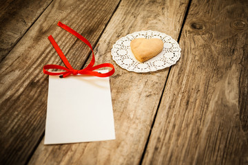 Valentine`s day. Cookies in the shape of a heart on a white napkin and white card on a wooden background, close up