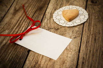 Valentine`s day. Cookies in the shape of a heart on a white napkin and white card on a wooden background, close up
