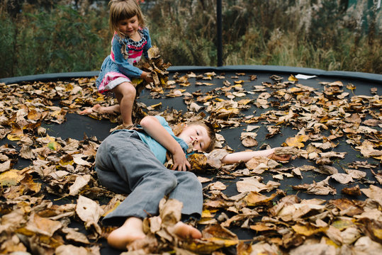 Siblings playing on trampoline with autumnal leaves 