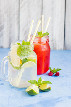Two cocktail - Summer drink, lemonade or mojito and Raspberry lemonade with mint, lemon, lime in a mason jars and ice on blue table background.
