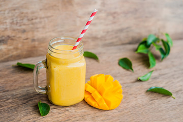 Juicy smoothie from mango in glass mason jar with striped red straw on old wooden background....