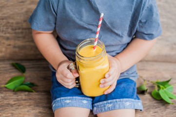 Boy drinking juicy smoothie from mango in glass mason jar with striped red straw on old wooden background. Healthy life concept, copy space © galitskaya
