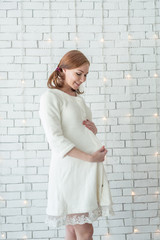 Young pregnant girl smiling and standing near white wall