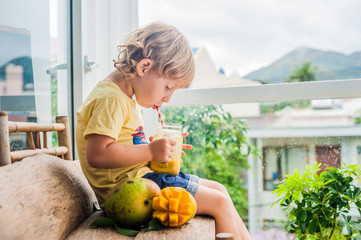 Boy drinking juicy smoothie from mango in glass mason jar with striped red straw on old wooden...