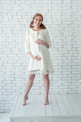 Young pregnant girl smiling and standing near white wall