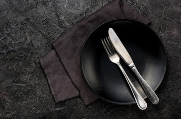 Fork, knife with napkin, roses and black plate. On dark table background.