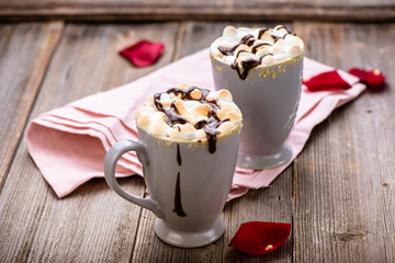 S'mores drink. Two mugs of hot chocolate with marshmallows on a wooden table. Cocoa. Rose petals. Valentine.