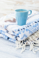 Warm plaid with blue pattern and blue cup of coffee on grey wooden background