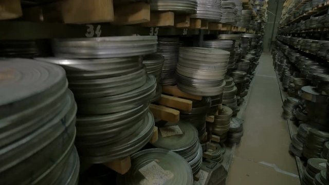 Old vintage film reel, film tapes in cases lying on archive shelfs. Dolly shot. 4K.
