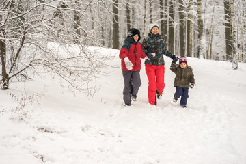 Happy mother having fun running in the winter forest with her tw