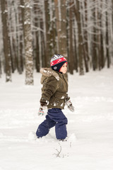 Fototapeta na wymiar Little boy goes through the deep snow in the winter forest
